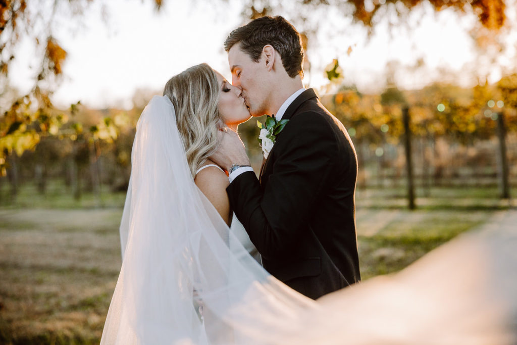 bride and groom share romantic sunset kiss during golden hour portraits in the vineyard at long hollow gardens