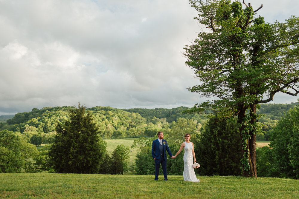 beautiful outdoor countryside wedding photo of couple holding hands with rolling hills and sunshine by nashville wedding photographer sara bill photography